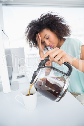 Tired businesswoman pouring a cup of coffee at desk