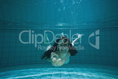 Pretty brunette smiling and offering her hand underwater