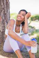 Fit woman sitting against tree holding water bottle