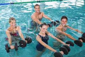 Happy fitness class doing aqua aerobics with foam dumbbells