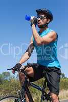 Handsome cyclist taking a break on his bike drinking water