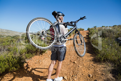 Fit cyclist carrying his bike on country terrain