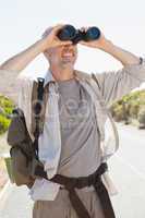 Hiker standing on road looking through binoculars