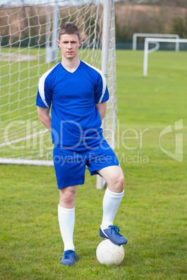 Football player in blue posing with the ball on pitch