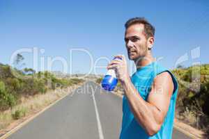 Athletic man on open road taking a drink