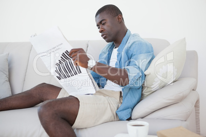 Casual man sitting on sofa reading the paper