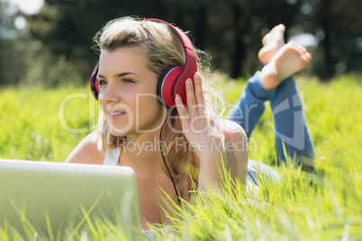 Pretty blonde lying on grass using laptop listening to music