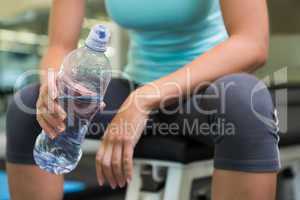 Fit woman sitting on bench holding water bottle