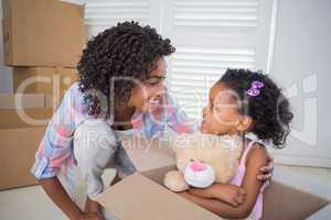 Cute daughter sitting in moving box holding teddy with mother
