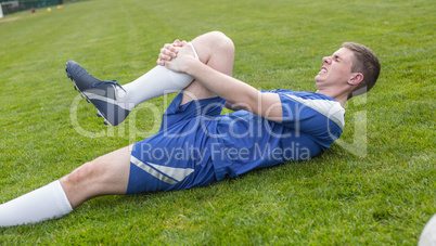 Football player in blue lying injured on the pitch