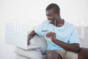 Casual man sitting on sofa using laptop to shop online
