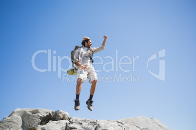 Handsome hiker jumping at the summit smiling at camera