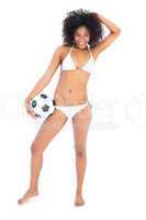 Beautiful fit girl in white bikini holding football smiling at c