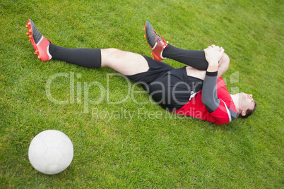 Football player in red lying injured on the pitch