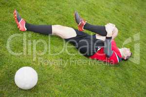 Football player in red lying injured on the pitch
