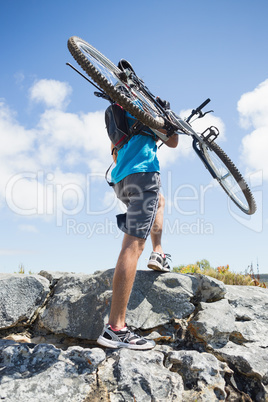 Fit man walking up rocky terrain holding mountain bike