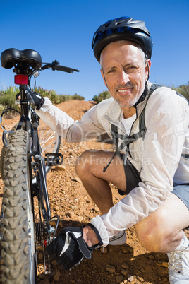 Smiing cyclist fixing his bike chain on country terrain