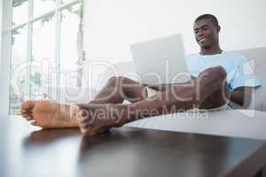 Casual man sitting on sofa using laptop with feet up