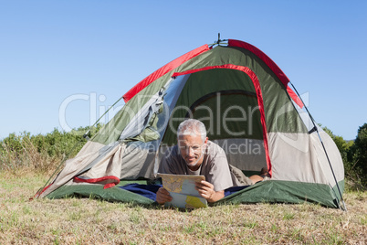 Happy camper looking at map lying in his tent Happy camper looking at map lying in his tent