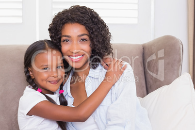 Pretty mother sitting on the couch with her daughter smiling at