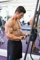 Shirtless muscular man using triceps pull down in gym