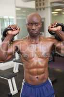 Muscular man lifting kettle bells in gym