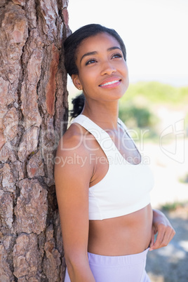 Fit woman leaning against tree smiling