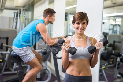 Fit brunette lifting weights smiling at camera