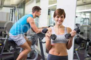 Fit brunette lifting weights smiling at camera