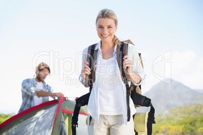 Attractive hiking blonde smiling at camera while partner pitches