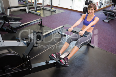 Fit smiling brunette working out on rowing machine