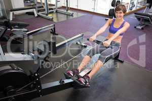 Fit smiling brunette working out on rowing machine