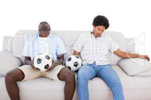 Distraught football fans sitting on the couch with balls
