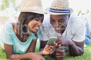 Happy couple lying in garden together looking at smartphone