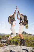 Hiking couple standing on mountain terrain cheering and jumping