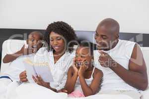 Family relaxing together in bed reading book
