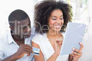 Attractive couple using tablet together on sofa to shop online