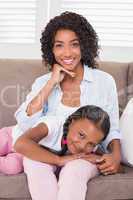 Pretty mother sitting on the couch with her daughter smiling at