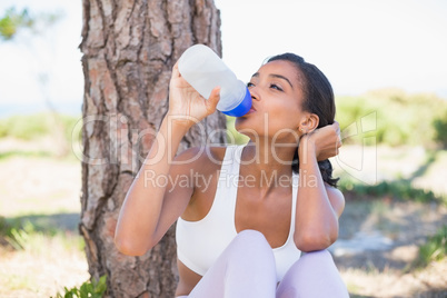 Fit woman sitting against tree drinking from water bottle