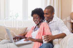 Cute couple relaxing on couch with laptop and coffee