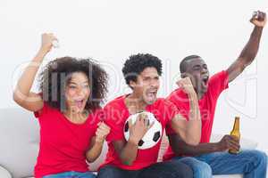 Football fans in red sitting on couch cheering