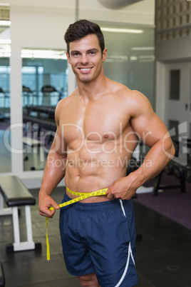 Shirtless muscular man measuring waist in gym