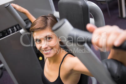 Happy brunette using weights machine for arms