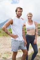Attractive fit couple standing on mountain trail smiling at came