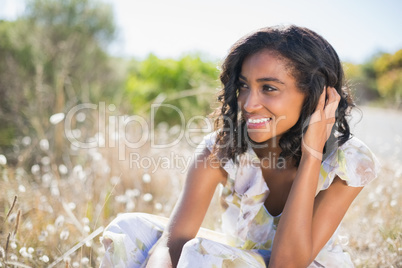 Happy pretty woman sitting on the grass in floral dress