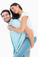 Happy casual man giving pretty girlfriend piggy back