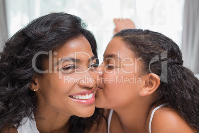 Pretty woman lying on bed with her daughter kissing cheek