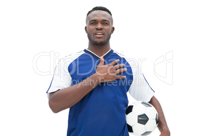 Football player in blue standing with the ball listening to anth