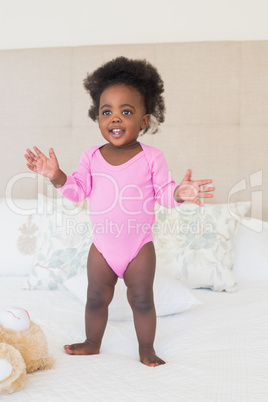 Baby girl in pink babygro standing on bed