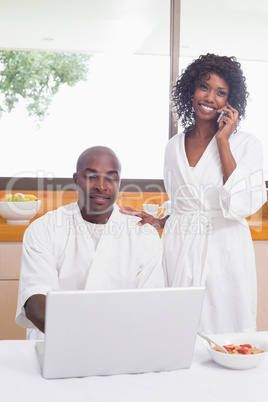 Happy couple in bathrobes in the kitchen using technology